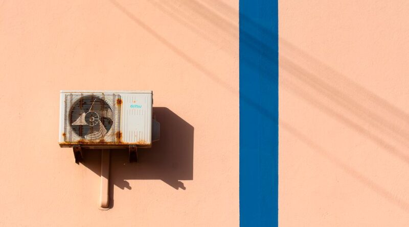 Rusty air conditioning unit casting shadow on a peach wall with blue stripe. - Photo by Jan van der Wolf on Pexels