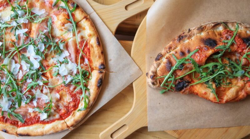 Freshly baked pizzas topped with prosciutto, arugula, and cheese, served on wooden boards. - Photo by Valeria Boltneva on Pexels